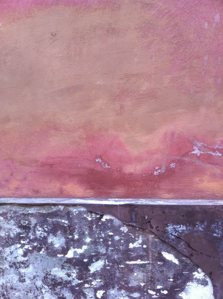 A wall in two registers: faded pink paint above, raw peeling plaster below, a ledge between.