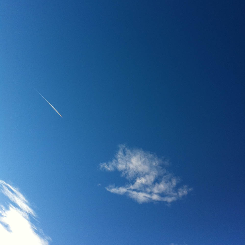 A thin contrail crossing deep blue sky above a small drifting cloud.